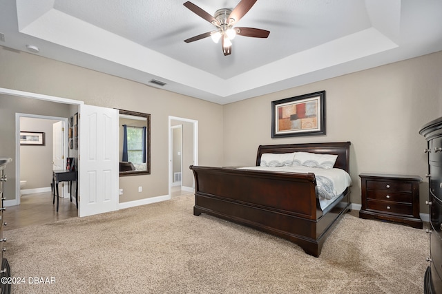 carpeted bedroom with ceiling fan and a raised ceiling