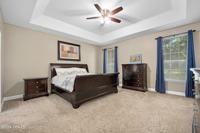 carpeted bedroom with ceiling fan and a tray ceiling