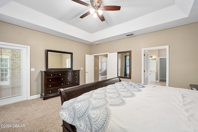 carpeted bedroom with ceiling fan, ensuite bath, and a tray ceiling