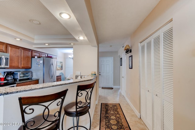 kitchen featuring a breakfast bar area, light stone countertops, a tray ceiling, kitchen peninsula, and stainless steel appliances