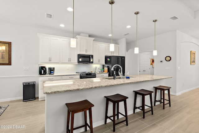 kitchen featuring white cabinetry, a kitchen island with sink, hanging light fixtures, and black appliances