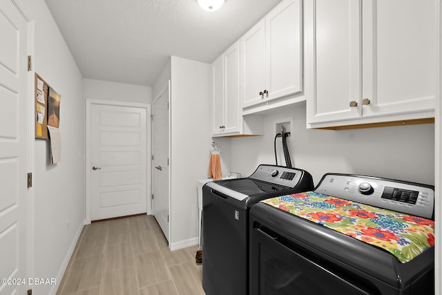 clothes washing area featuring cabinets, a textured ceiling, and washing machine and dryer