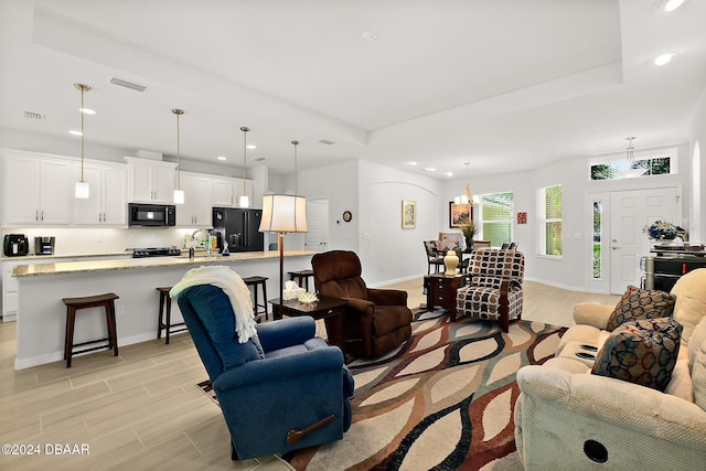 living room featuring a chandelier, light hardwood / wood-style floors, a raised ceiling, and sink