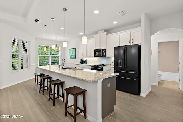 kitchen with light stone countertops, decorative light fixtures, a kitchen island with sink, white cabinets, and black appliances