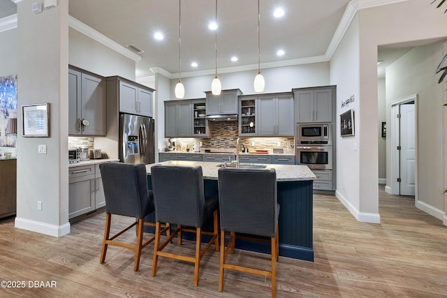 kitchen featuring appliances with stainless steel finishes, decorative light fixtures, tasteful backsplash, light stone countertops, and a center island with sink