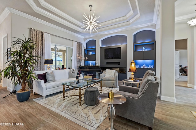 living room with built in shelves, ornamental molding, a tray ceiling, and hardwood / wood-style flooring