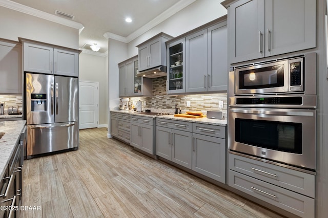 kitchen with light stone counters, backsplash, ornamental molding, and stainless steel appliances