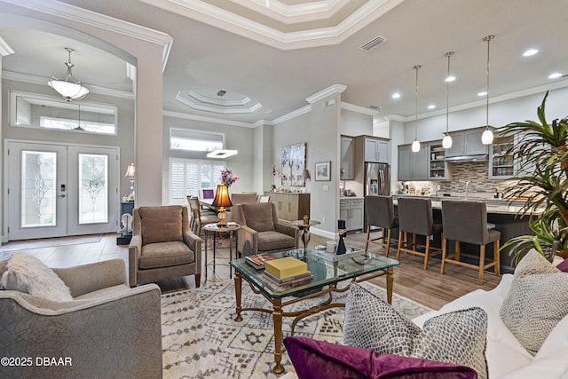 living room featuring a tray ceiling, crown molding, light hardwood / wood-style floors, and french doors