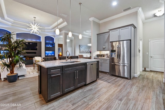 kitchen with sink, hanging light fixtures, appliances with stainless steel finishes, an island with sink, and light stone countertops