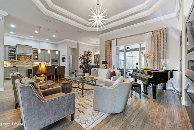 living room featuring crown molding, hardwood / wood-style floors, a tray ceiling, and ceiling fan with notable chandelier