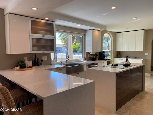 kitchen with light stone counters, black electric stovetop, white cabinetry, sink, and a breakfast bar