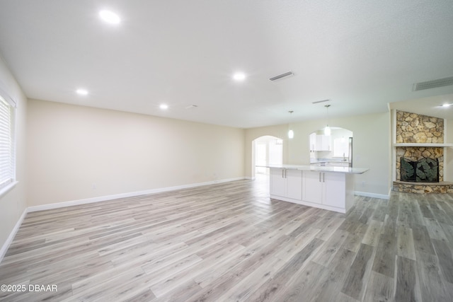 unfurnished living room featuring a healthy amount of sunlight, light hardwood / wood-style floors, and a stone fireplace