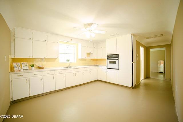 kitchen featuring oven, backsplash, finished concrete flooring, a ceiling fan, and light countertops
