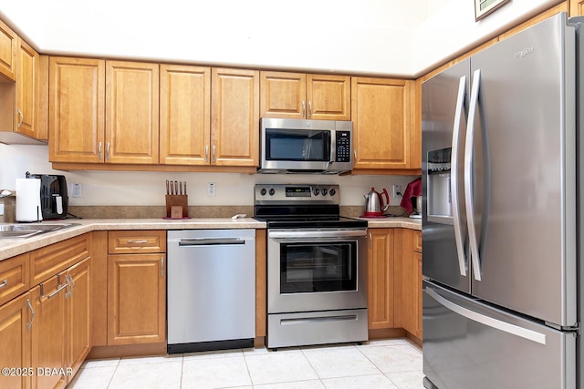 kitchen featuring a sink, light countertops, light tile patterned flooring, and stainless steel appliances