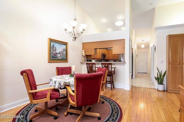 dining space with baseboards, a notable chandelier, high vaulted ceiling, and light wood finished floors