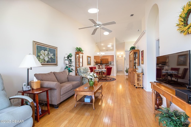 living area with ceiling fan with notable chandelier, light wood-style floors, arched walkways, and high vaulted ceiling