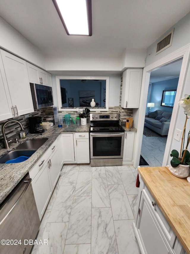 kitchen with stainless steel appliances, light stone counters, white cabinets, decorative backsplash, and sink