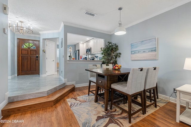 dining space with crown molding, light hardwood / wood-style flooring, a textured ceiling, and an inviting chandelier