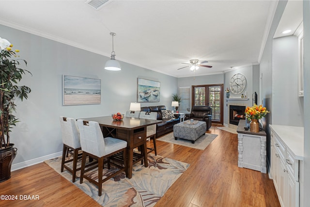 dining space featuring ceiling fan, a fireplace, ornamental molding, and light wood-type flooring