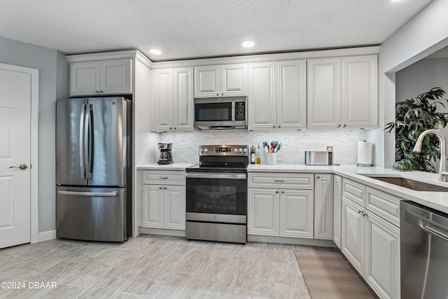 kitchen featuring sink, stainless steel appliances, a textured ceiling, decorative backsplash, and white cabinets