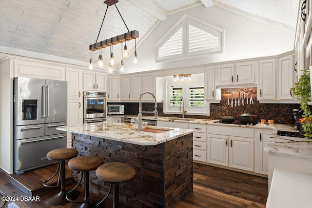 kitchen with beam ceiling, high vaulted ceiling, an island with sink, decorative light fixtures, and appliances with stainless steel finishes