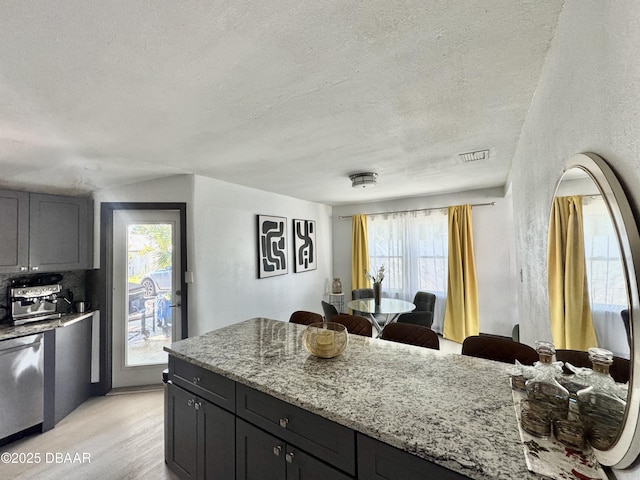 326 Ribault Ave, Daytona Beach, FL 32118 - kitchen featuring a textured ceiling, stainless steel dishwasher, light stone counters, light wood finished floors, and visible vents