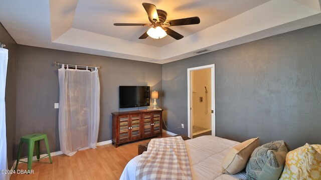 bedroom featuring ensuite bathroom, light hardwood / wood-style floors, ceiling fan, and a raised ceiling