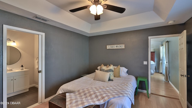 bedroom with a raised ceiling, ensuite bathroom, sink, ceiling fan, and light hardwood / wood-style flooring