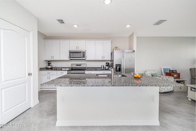 58 Bella Oaks Dr, Port Orange, FL 32129 - kitchen with stainless steel appliances, dark stone countertops, a center island with sink, white cabinets, and light tile patterned flooring
