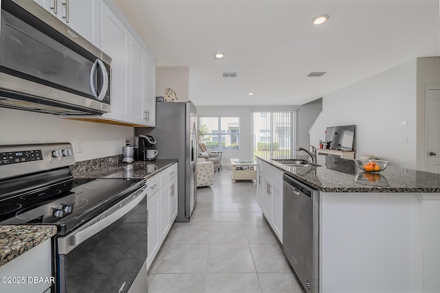 58 Bella Oaks Dr, Port Orange, FL 32129 - kitchen featuring appliances with stainless steel finishes, white cabinets, a center island with sink, light tile patterned flooring, and dark stone countertops