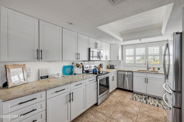 5499 S Atlantic Ave, New Smyrna Beach, FL 32169 - kitchen with appliances with stainless steel finishes, white cabinetry, tasteful backsplash, a raised ceiling, and light stone countertops