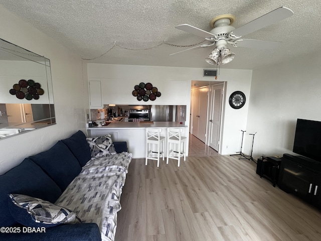 living room with ceiling fan, light wood-type flooring, and a textured ceiling