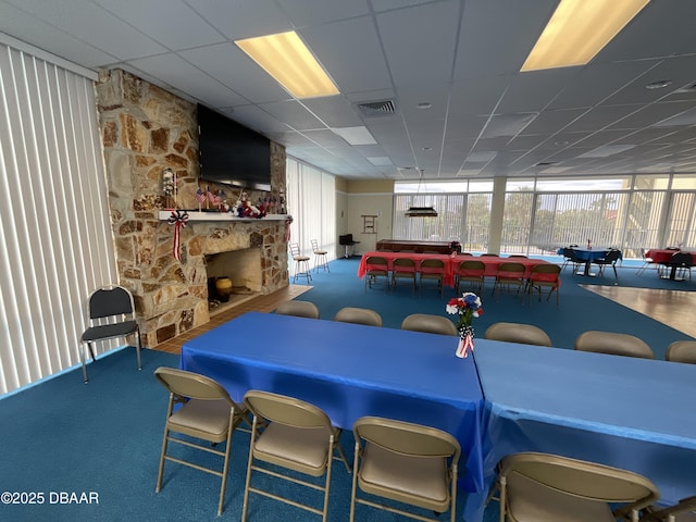 carpeted dining area with a paneled ceiling and a fireplace