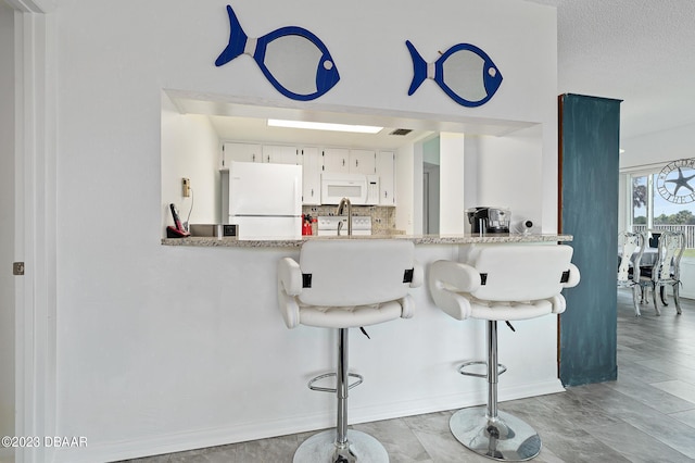 3600 S Ocean Shore Blvd # 111, Flagler Beach, FL 32136 - kitchen featuring a peninsula, white appliances, a kitchen breakfast bar, white cabinetry, and decorative backsplash