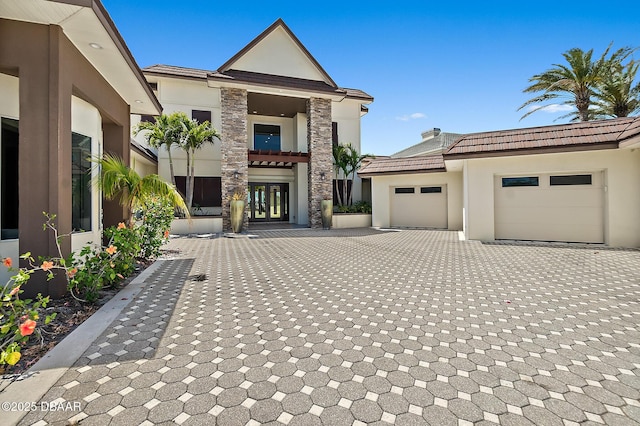view of front of house with an attached garage, a tile roof, stone siding, stucco siding, and decorative driveway