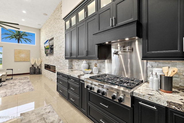 kitchen with light tile patterned flooring, glass insert cabinets, tasteful backsplash, dark cabinetry, and stainless steel gas stovetop