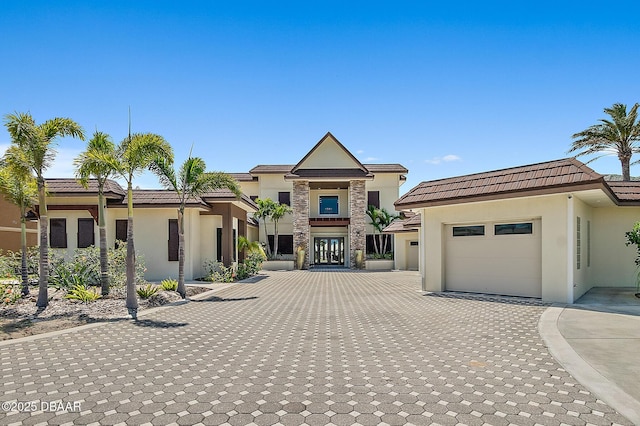 view of front facade featuring decorative driveway, an attached garage, stone siding, and stucco siding