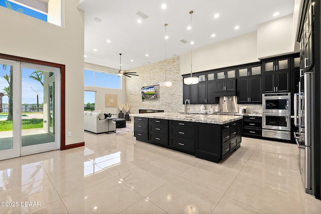 kitchen with a towering ceiling, appliances with stainless steel finishes, dark cabinets, tasteful backsplash, and a warming drawer