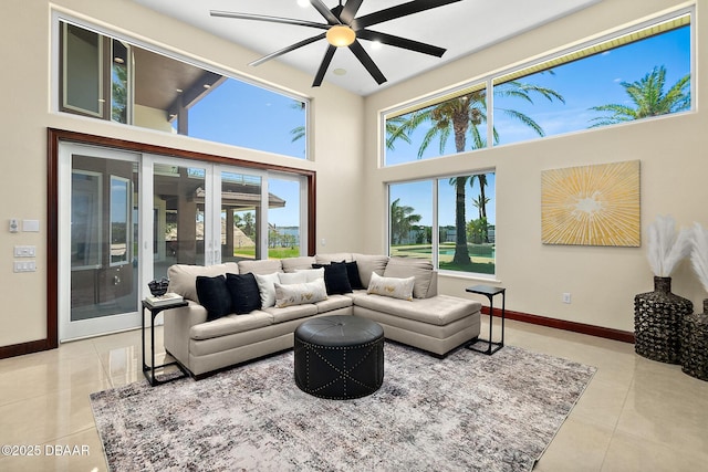 living room with baseboards, tile patterned flooring, ceiling fan, and a towering ceiling