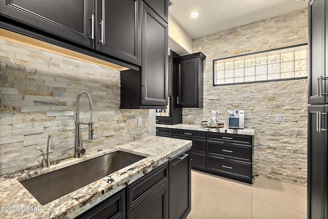 kitchen with dark cabinets, a sink, light tile patterned floors, and light stone counters