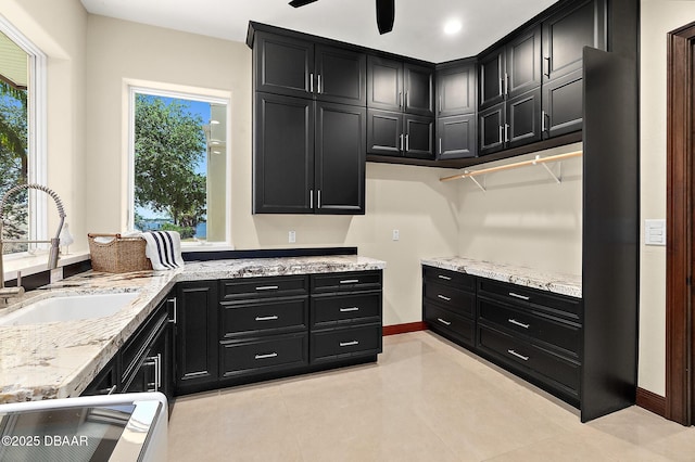 kitchen featuring a sink, dark cabinetry, light stone countertops, and plenty of natural light