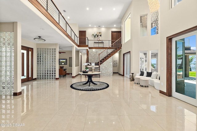 foyer with baseboards, a towering ceiling, light tile patterned floors, and stairway