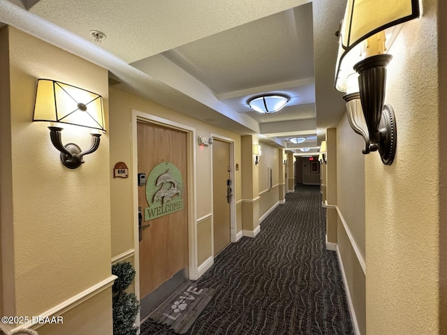 hall with dark colored carpet, baseboards, a textured ceiling, and a textured wall