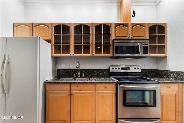 kitchen featuring appliances with stainless steel finishes, glass insert cabinets, a sink, and dark stone countertops