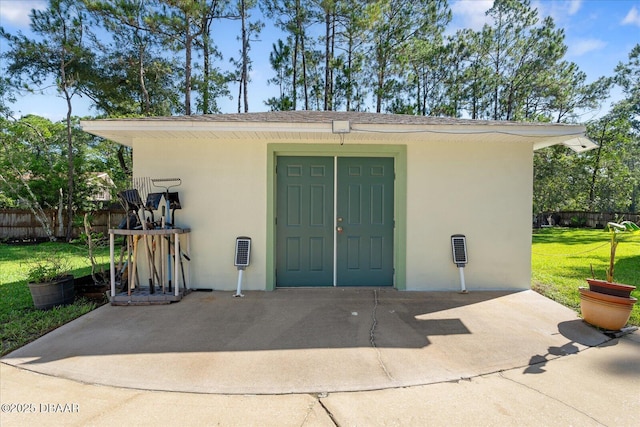 entrance to property featuring fence, a lawn, and stucco siding