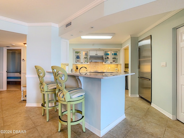 kitchen with crown molding, stainless steel refrigerator, white cabinets, a breakfast bar area, and kitchen peninsula