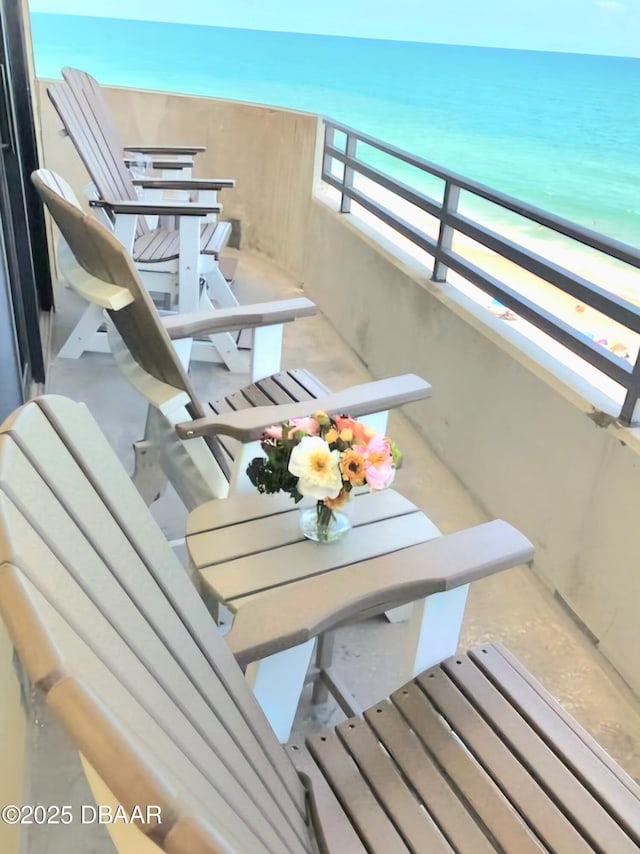 balcony with outdoor dining space, a water view, and a view of the beach