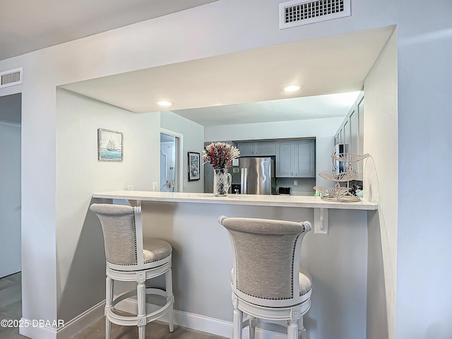 kitchen featuring baseboards, stainless steel fridge, visible vents, and a breakfast bar area