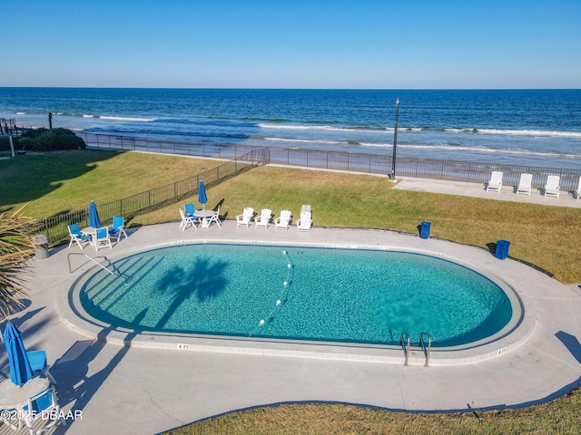 community pool featuring a patio area, a water view, fence, and a view of the beach