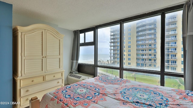 bedroom featuring a water view, a wall of windows, a textured ceiling, and a wall unit AC